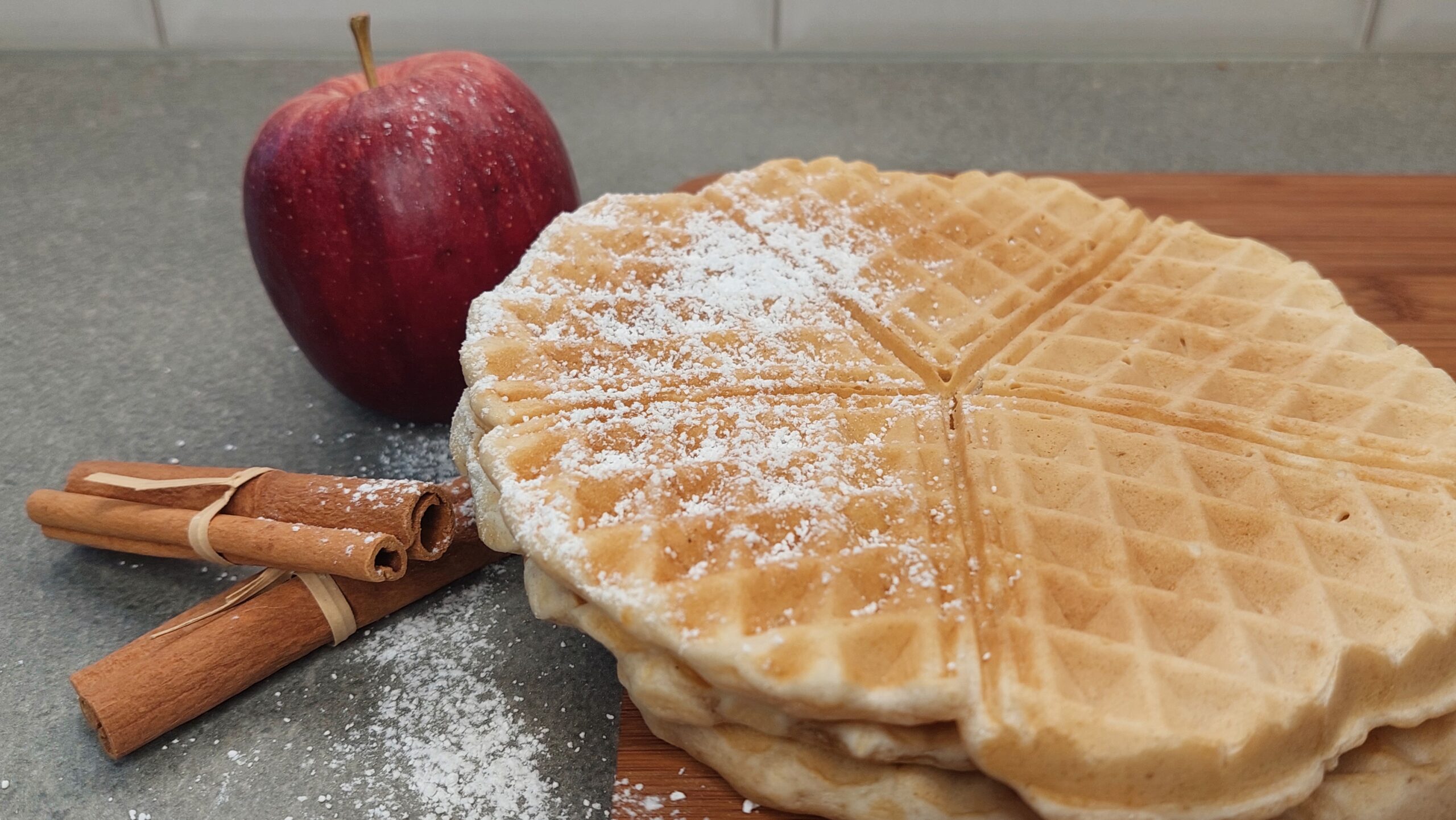 Waffeln ohne Zucker bestreut mit Puderzucker mit Apfel und Zimtstangen daneben
